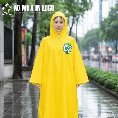 Một cô gái trẻ người Việt Nam mặc áo mưa cài cạnh màu vàng C2 đứng trên vỉa hè phố dưới trời mưa
