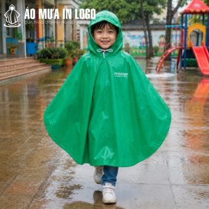 Bé trai mặc chiếc áo mưa poncho màu xanh lá cây tự tin đi bộ dưới trời mưa tại sân trường