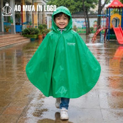 Bé trai mặc chiếc áo mưa poncho màu xanh lá cây tự tin đi bộ dưới trời mưa tại sân trường