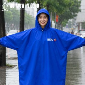 Nữ nhân viên công sở mỉm cười rạng rỡ trải nghiệm áo mưa dáng bít màu xanh dương đậm dưới trời mưa lớn.
